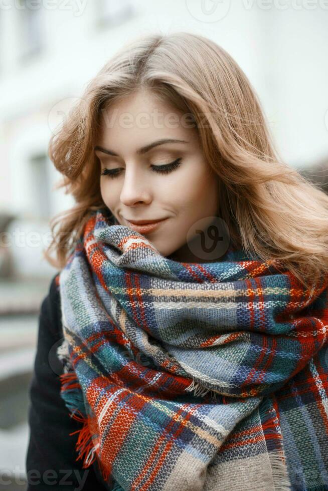 Cute young woman in trendy knitted scarf and black coat in autumn day photo