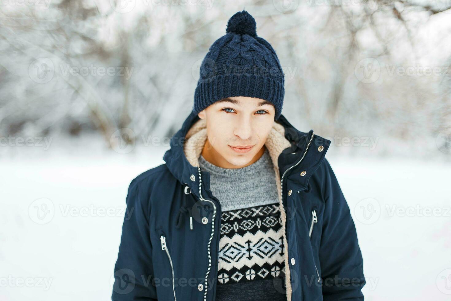 hermoso joven hombre en invierno chaqueta, de punto suéter con un modelo y un de punto sombrero caminando en un invierno parque foto