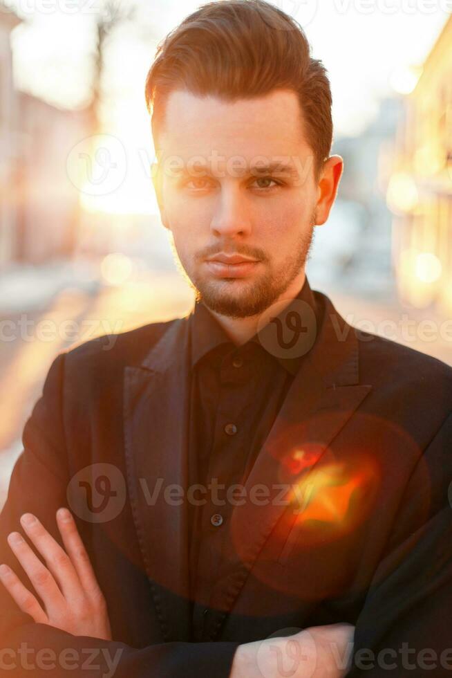 Handsome man with a beard and hairstyle in black elegant suit at sunset photo
