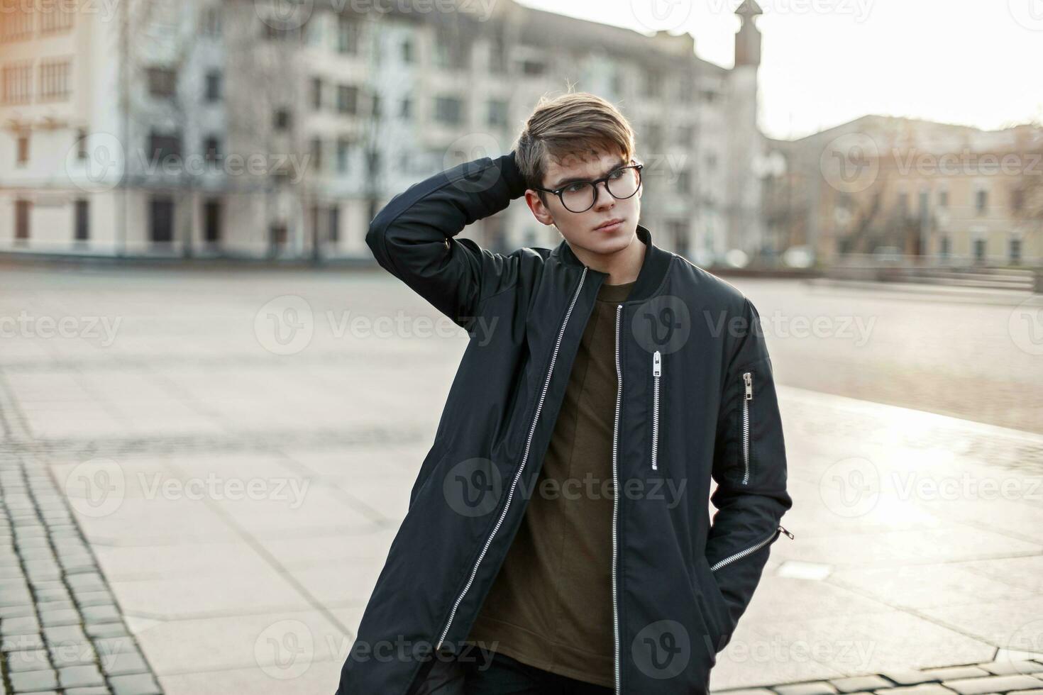 Fashionable young man with a haircut in a black jacket walking in the city photo