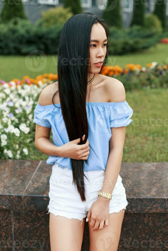 Vietnamese Beautiful woman with long hair in a blue blouse posing in park near flowers. photo