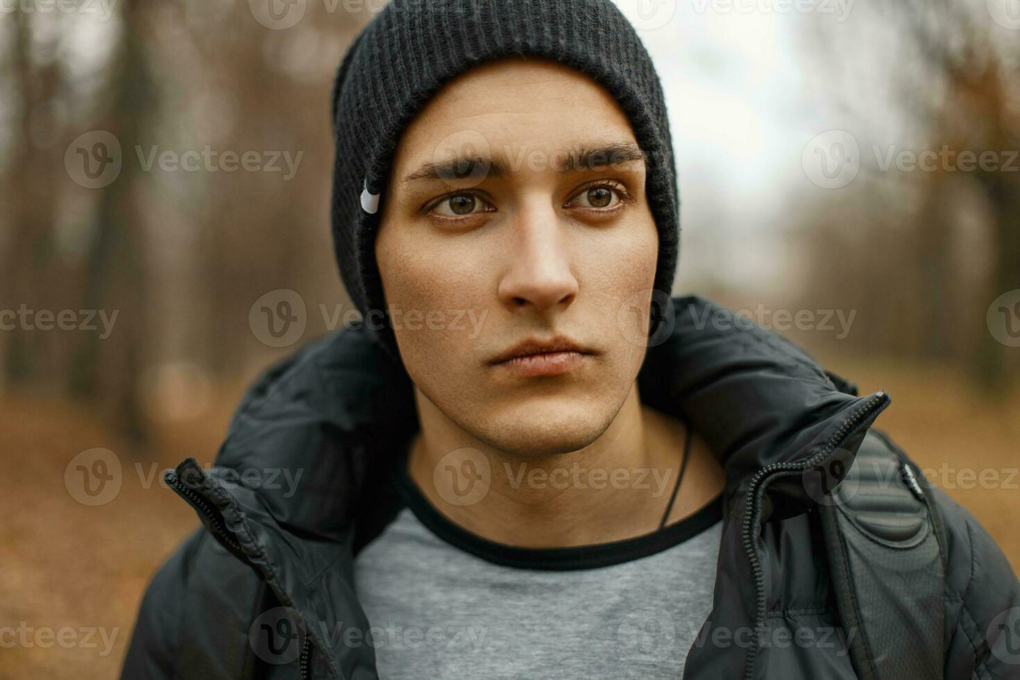 Portrait of a handsome man in a black knitted hat and winter jacket in the autumn park. photo