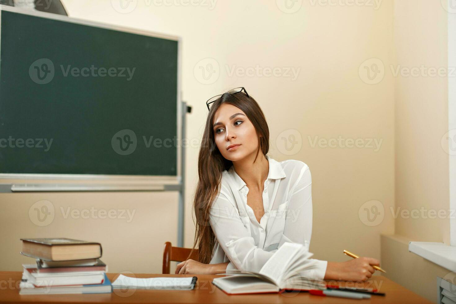 Beautiful young woman sitting at the table with books near blackboard photo