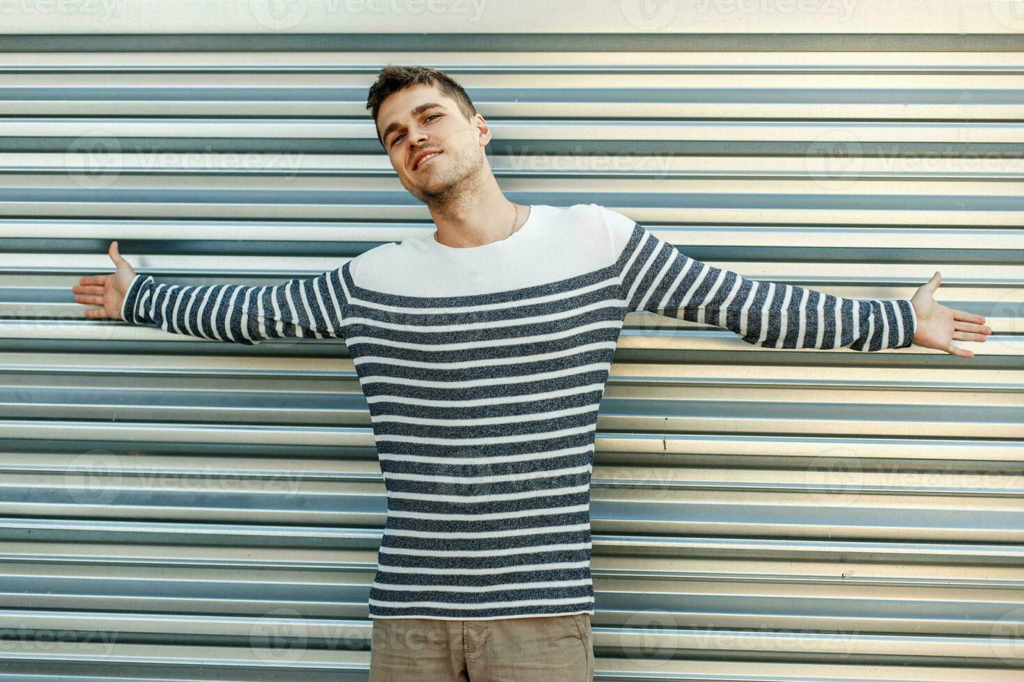 joven hombre en un suéter indefenso gesto cerca el metal pared foto