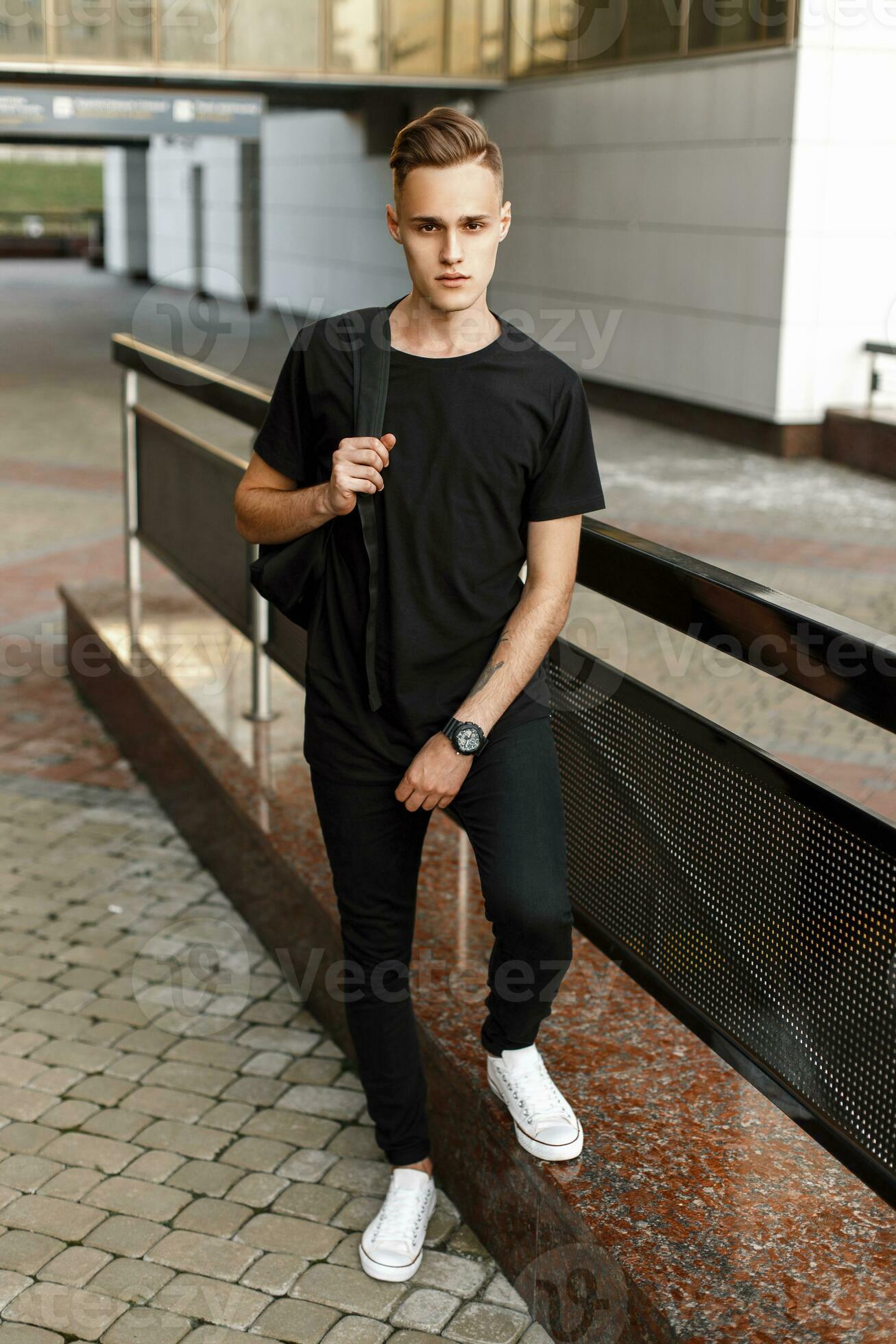 Onset Ryd op fatning Handsome hipster man in stylish black t-shirt, pants and white sneakers  with a backpack standing near the modern building. 23334675 Stock Photo at  Vecteezy