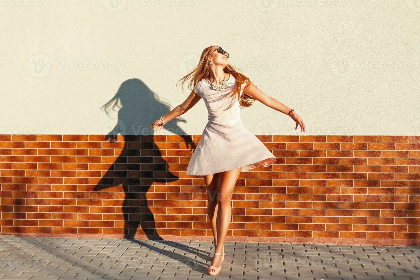 Beautiful young cheerful woman with a smile in a pink dress is spinning around itself near the wall. Happy girl having fun photo