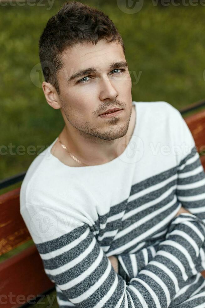 retrato de hermoso hombre descansando en un banco en el parque. foto