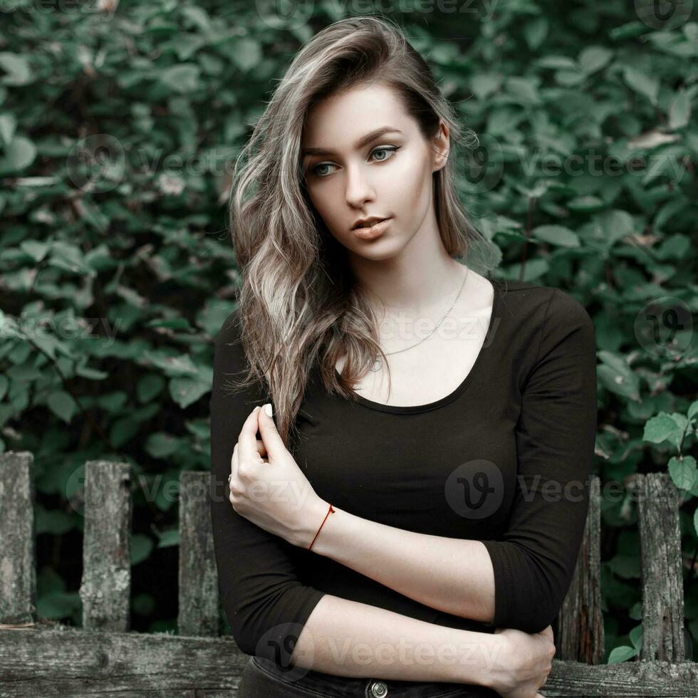 retrato de un hermosa país niña en un negro camiseta cerca el verde follaje foto