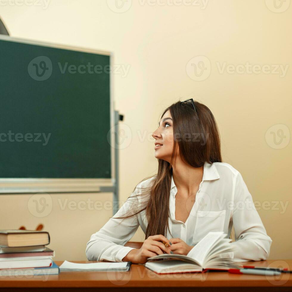 Beautiful young girl in white blouse looks at the chalkboard photo