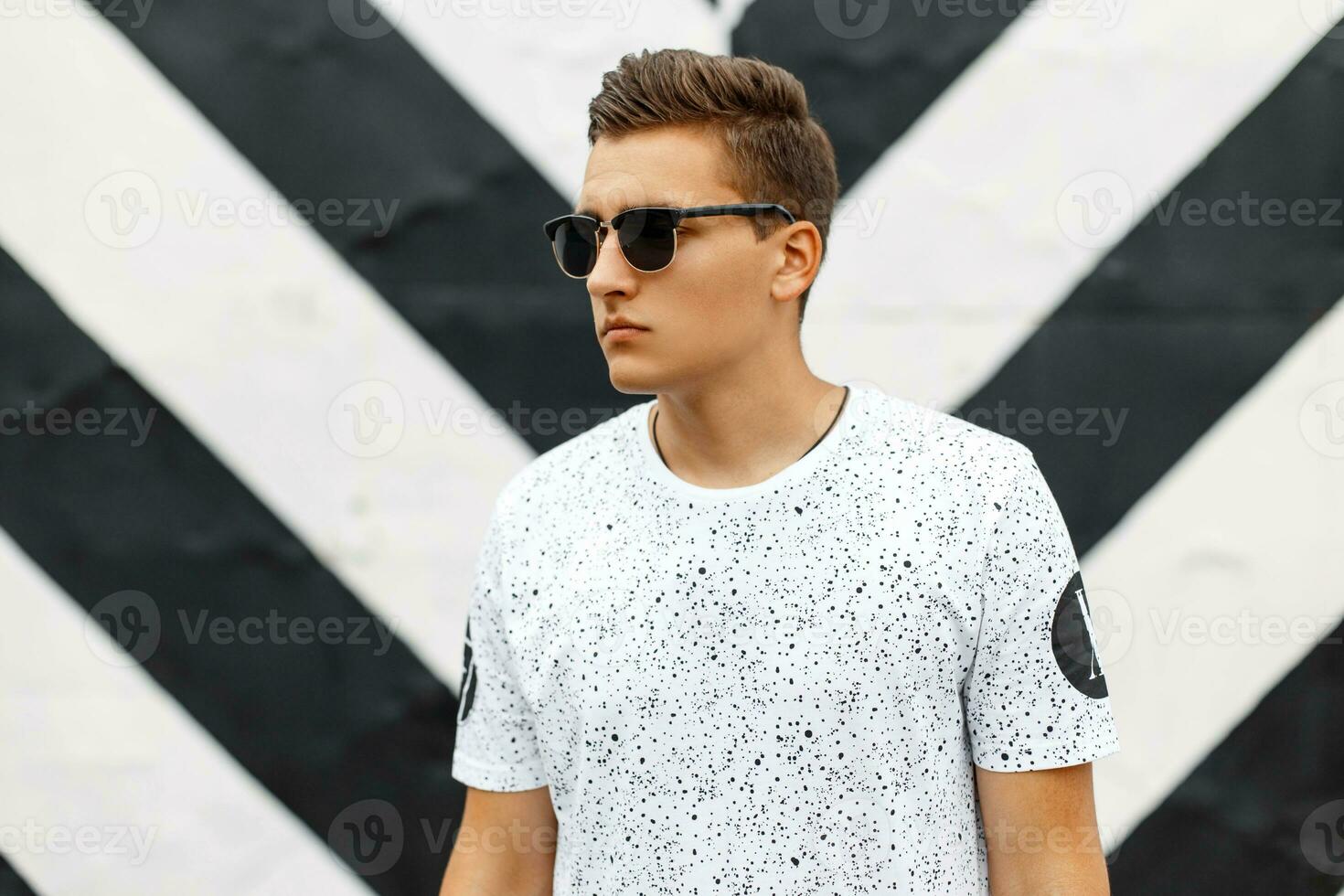 Handsome man in sunglasses and a white T-shirt with spots on a background of black and white lines. photo