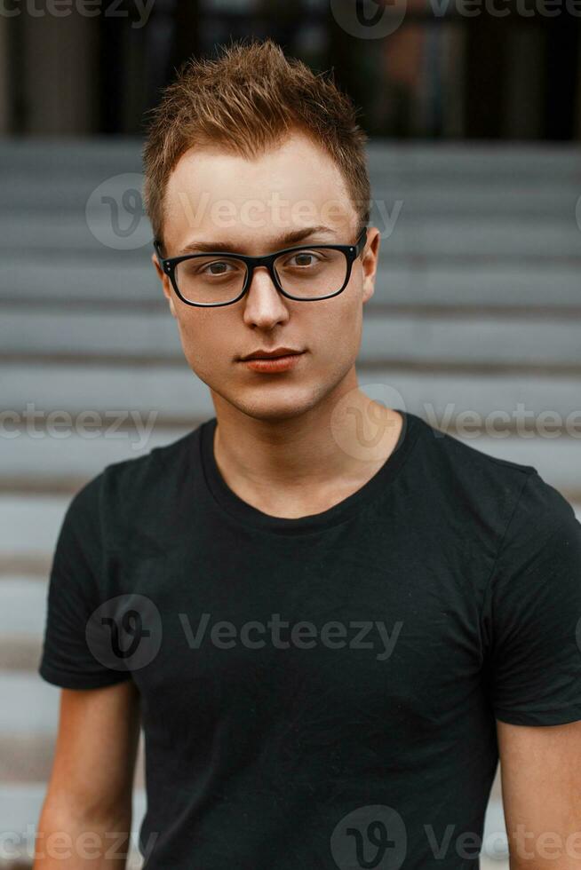 Beautiful stylish young guy in a black shirt and hipster glasses. photo