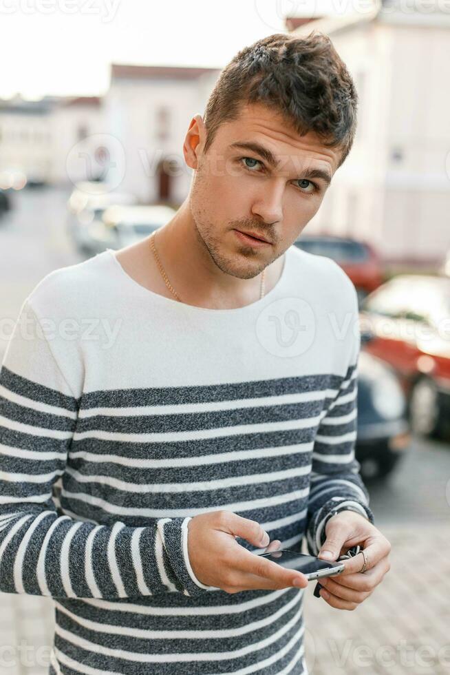 Handsome young man in a sweater keeps your phone. photo