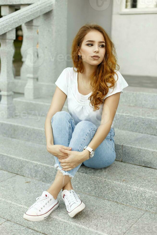 Young Pretty Woman in fashionable clothes sitting on the stairs at home photo