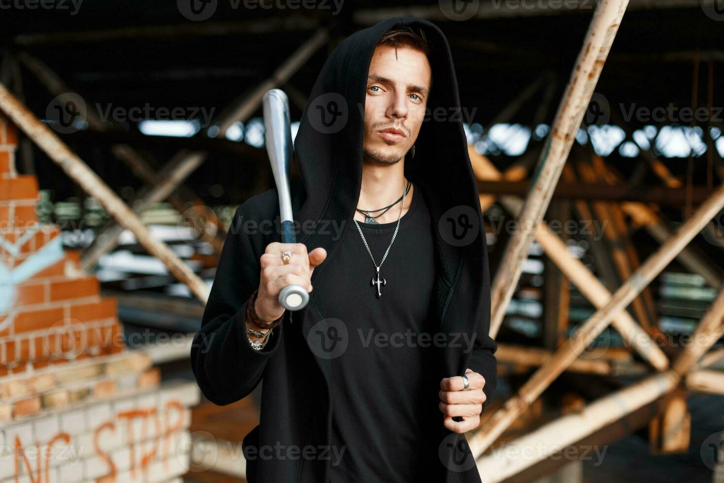 Trendy man with a hood holds a bat on the background of the old buildings photo