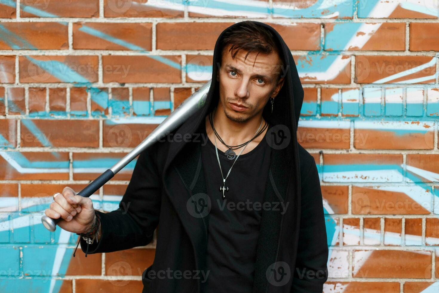 Angry guy near brick wall with graffiti holding a metal bat photo