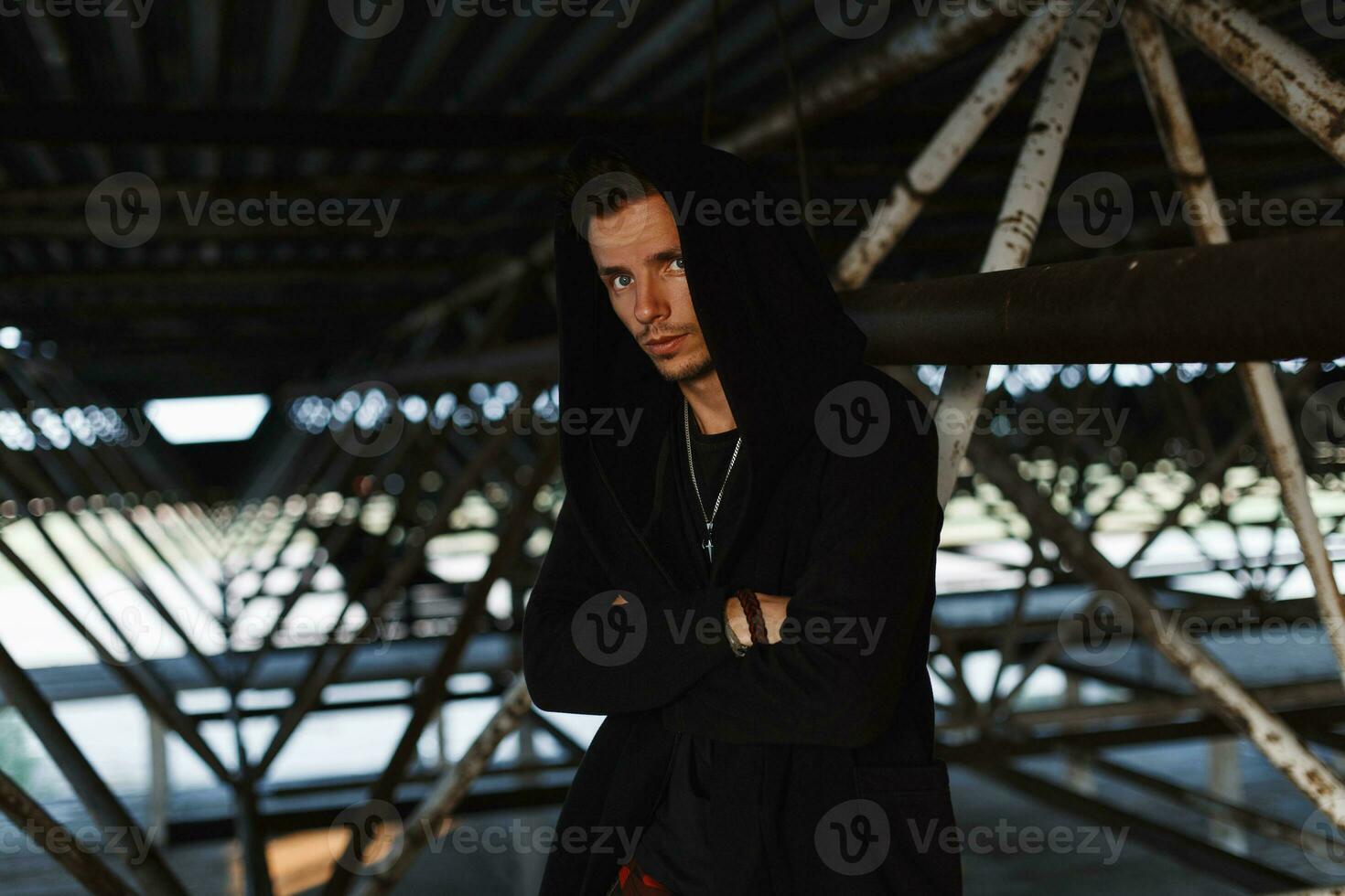 Handsome fashionable man in a stylish robes with a hood near metal structures photo