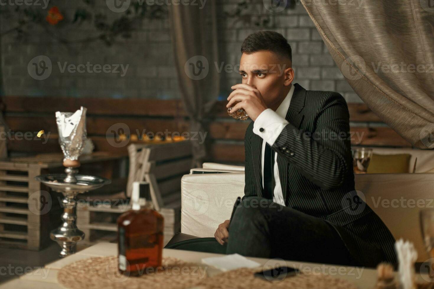 Handsome young man in a suit drinking whiskey in the modern bar photo