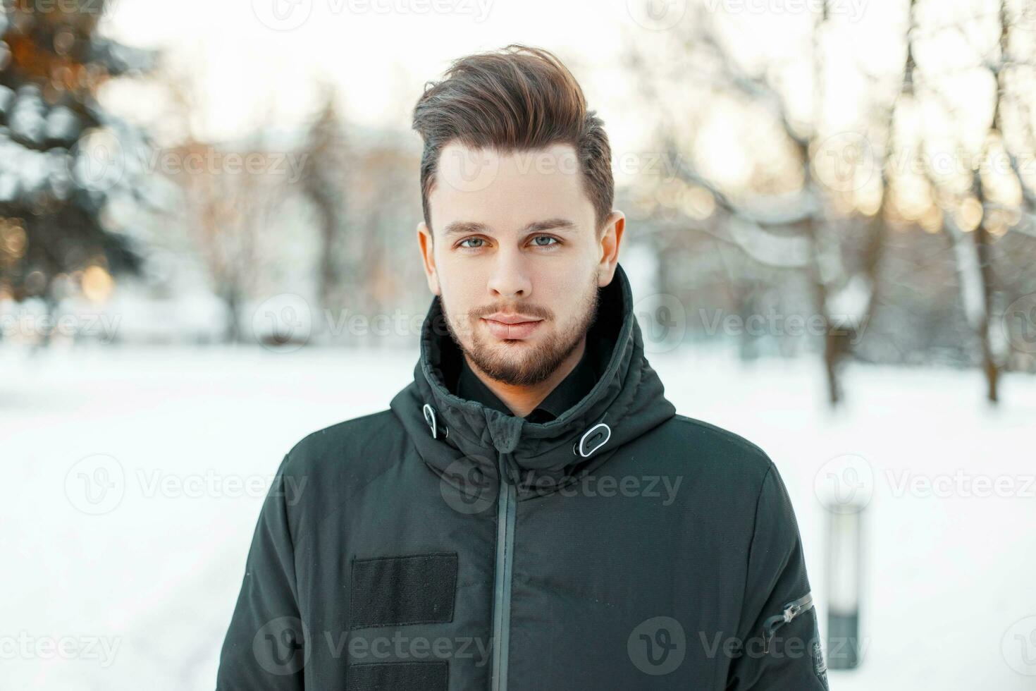 Handsome man with a beard and hairstyle in winter jacket in the park photo