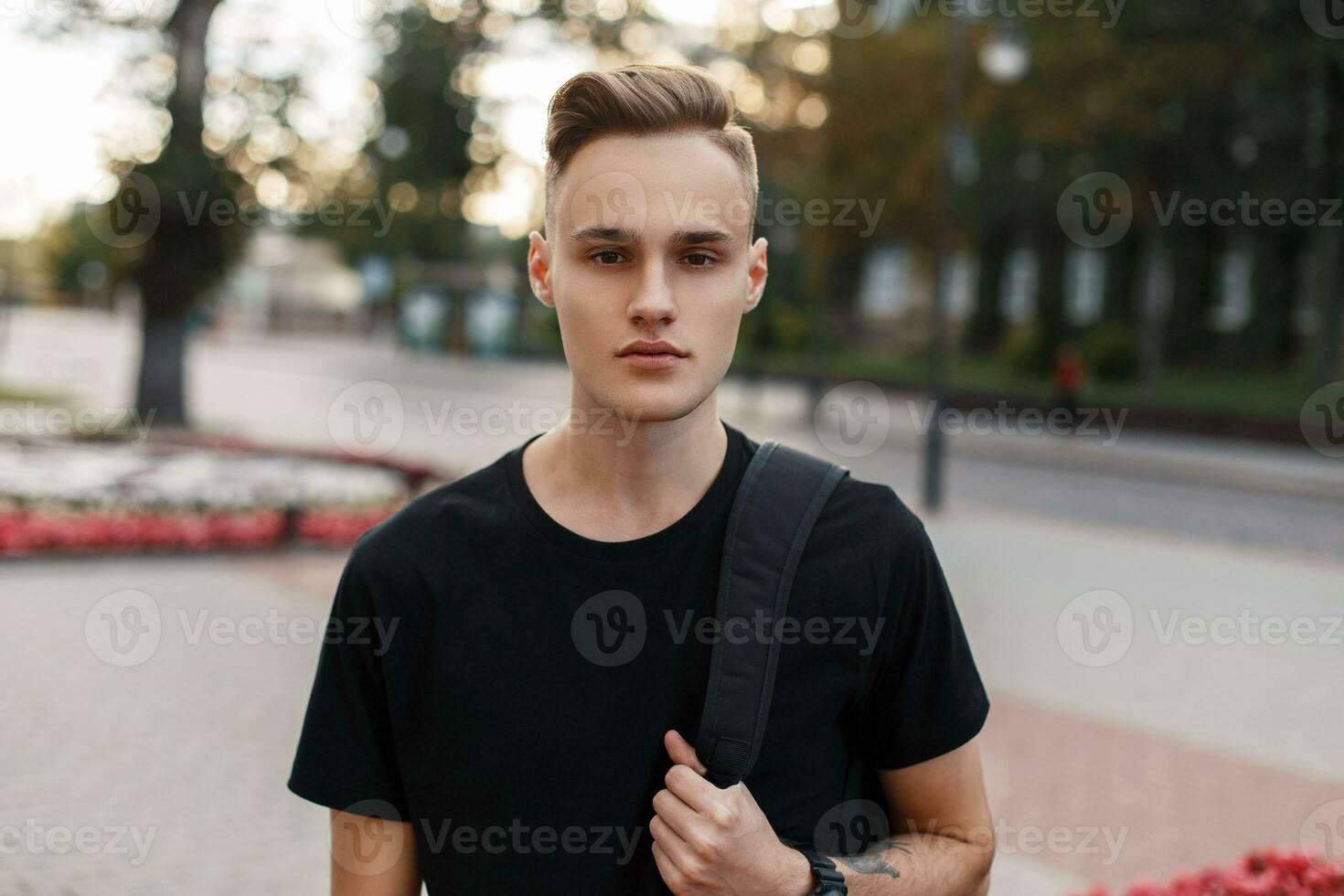 Handsome young man with a haircut with a backpack on the background of the city. photo