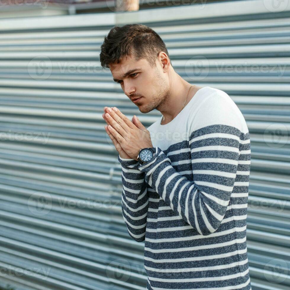 hermoso joven hombre en un suéter posando cerca un metal pared en un soleado día. foto