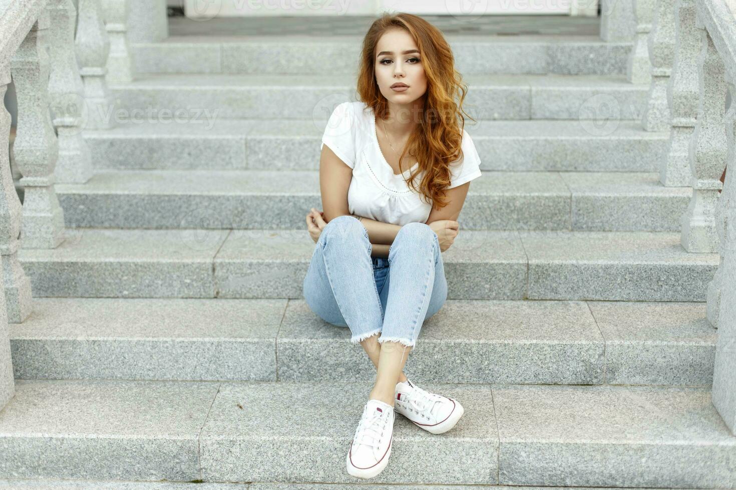 Young beautiful girl in a white T-shirt, jeans and shoes on the steps photo