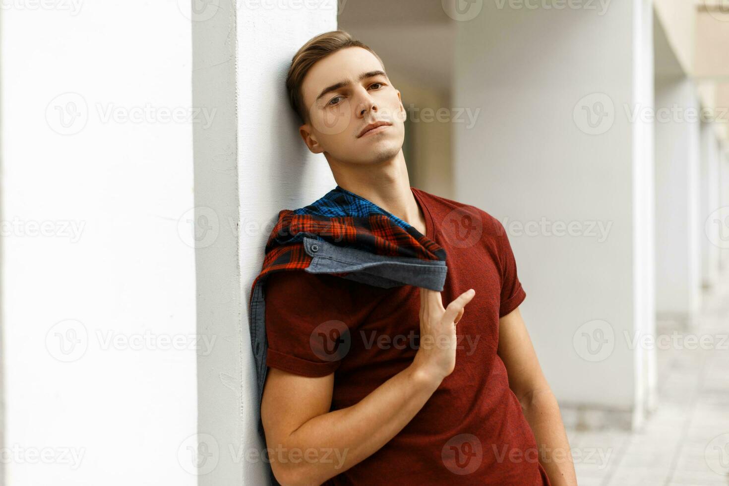 Handsome young guy with a haircut rests in the city. poses near the wall photo