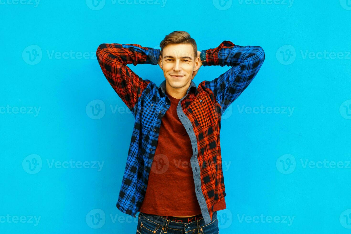 Handsome happy young man in fashionable jacket near a bright blue wall photo