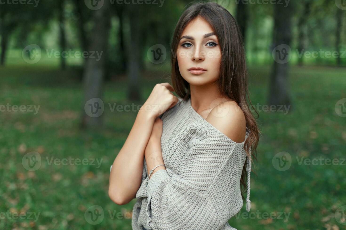 Beautiful young woman with a pretty face in a gray sweater in the park photo