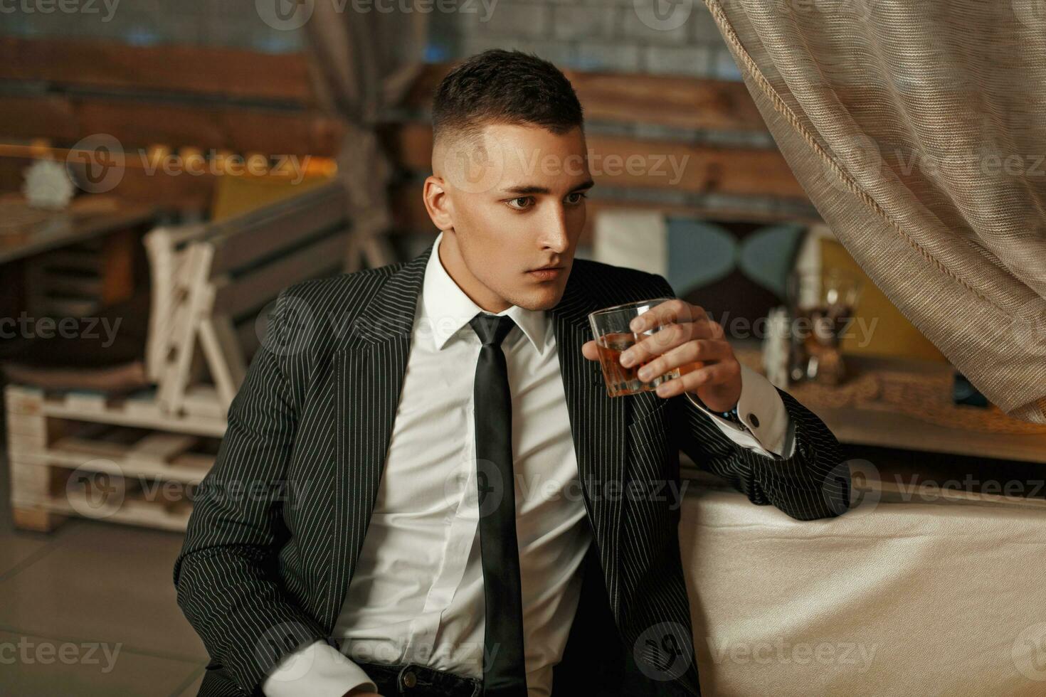 Young handsome man in a stylish suit drinking whiskey. photo