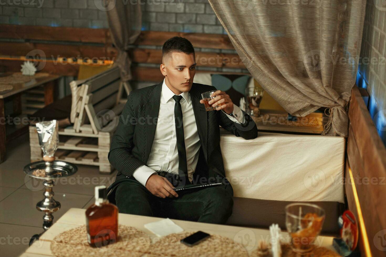 Young man in a suit drinks alcohol and smokes a hookah. photo