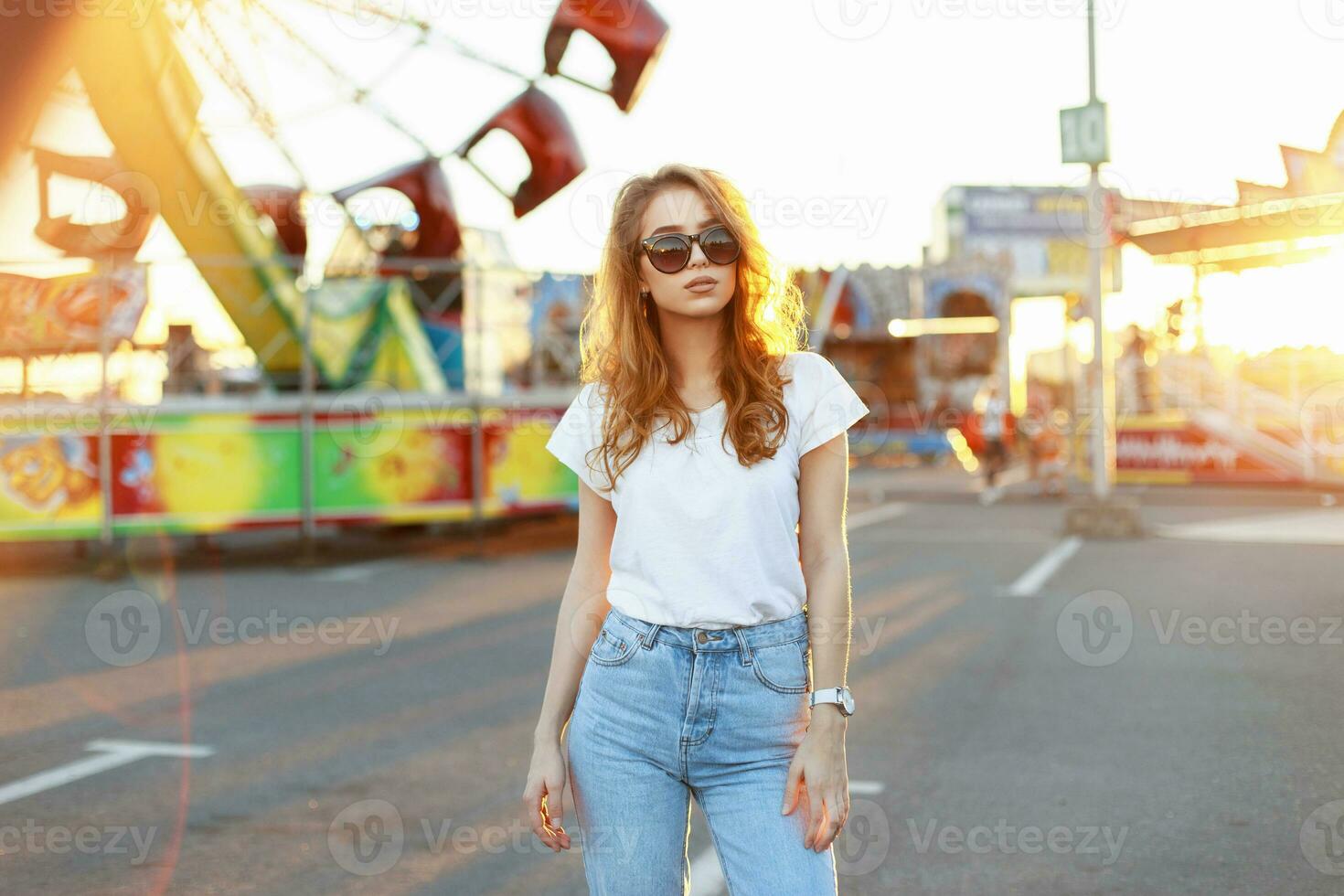 Beautiful young stylish woman in sunglasses walking in the amusement park at sunset. photo