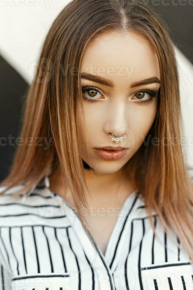 Modern portrait of a young beautiful girl with earrings in the nose in a striped blouse. Amazing eyes photo