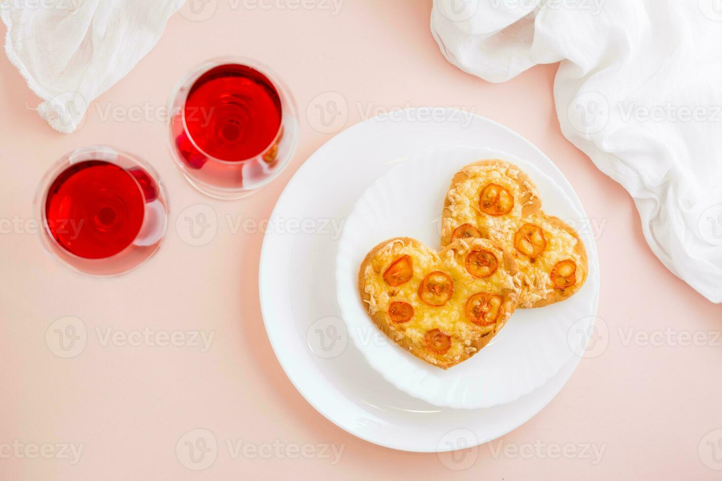 Two delicious heart-shaped pizzas on plates and two glasses of wine on a set table to celebrate valentine's day. Top view. Copy space photo