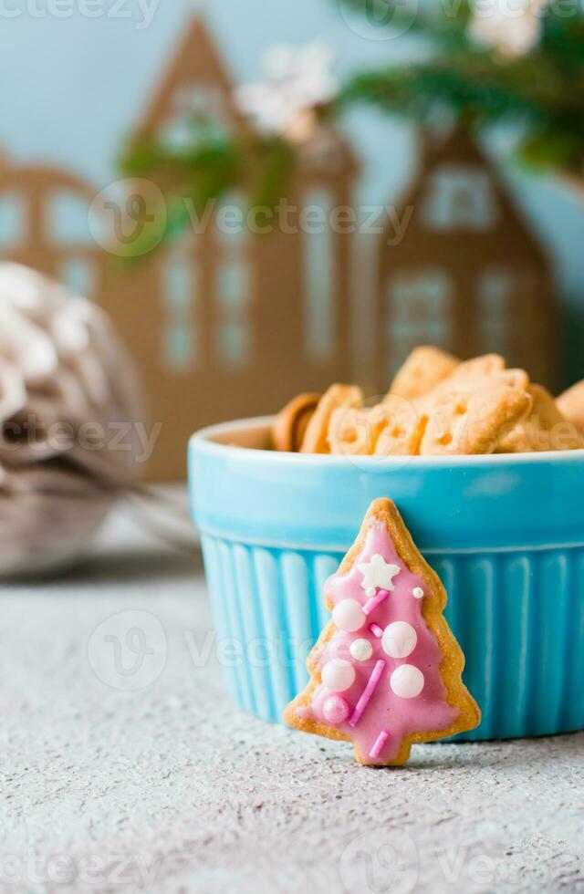 Christmas cookies spruce with pink icing are placed near a bowl of cookies on a decorated table. Festive treat. Vertical view. Close-up photo