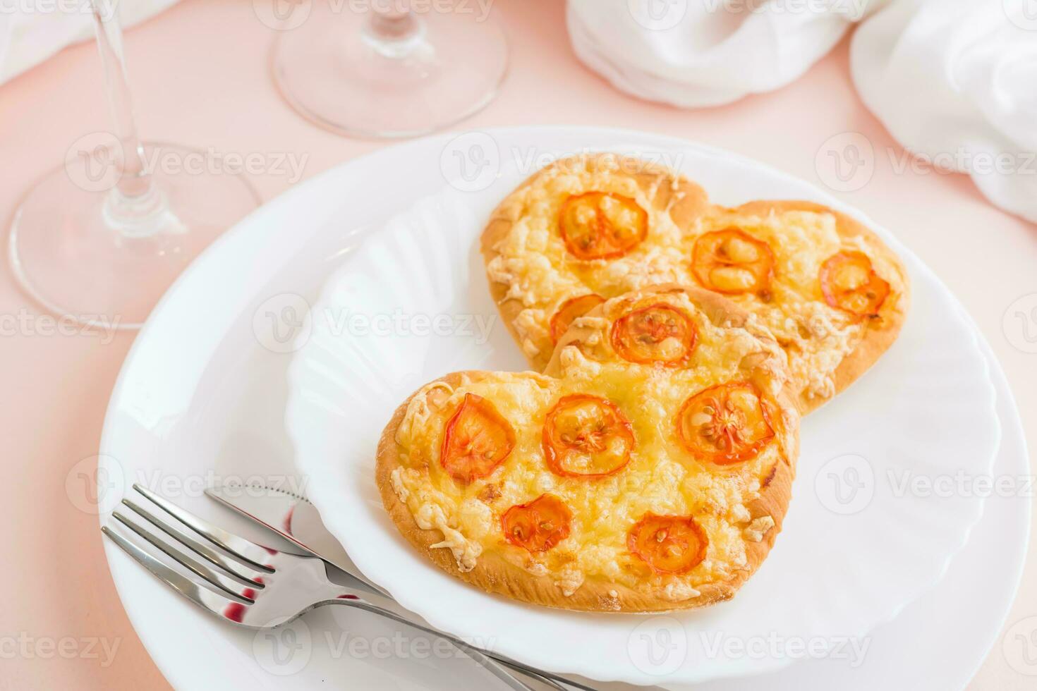 Two fresh pizzas in the shape of a heart on plates on a pink background. Valentine's Day. Close-up photo