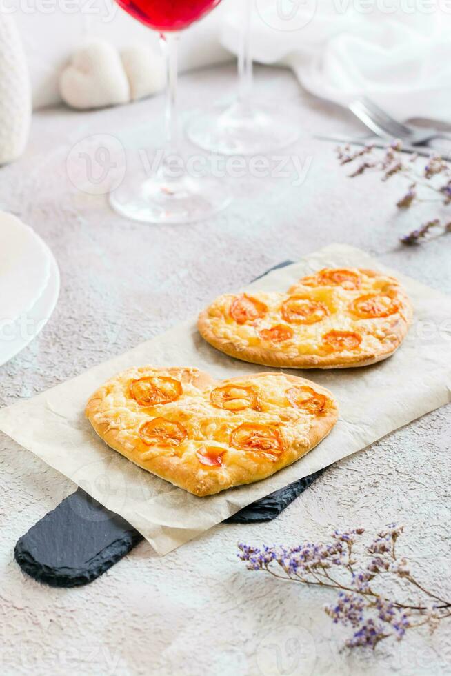 dos corazón conformado listo para comer pizzas en papel en conjunto mesa para San Valentín día celebracion. de cerca. vertical ver foto