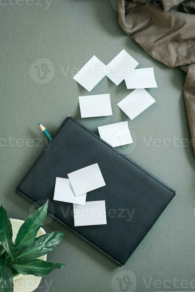 Green concept. Notepad, sheets for writing and fresh leaves in a coffee cup on a green background. Top and vertical view photo