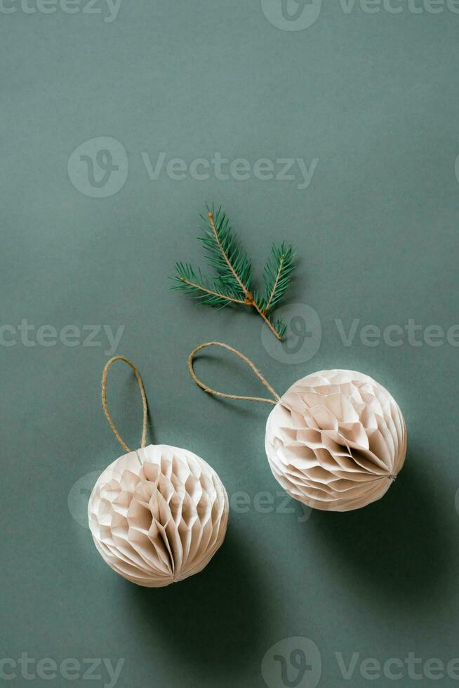 Two Christmas textured folded balls made of craft paper a branch of fir on a green background. Vertical view photo