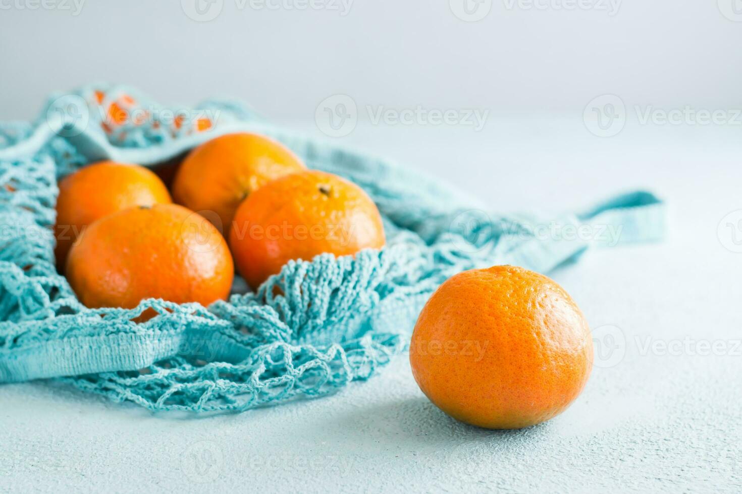 Ripe tangerines in a mesh bag on a blue background. Fruit in sustainable packaging photo