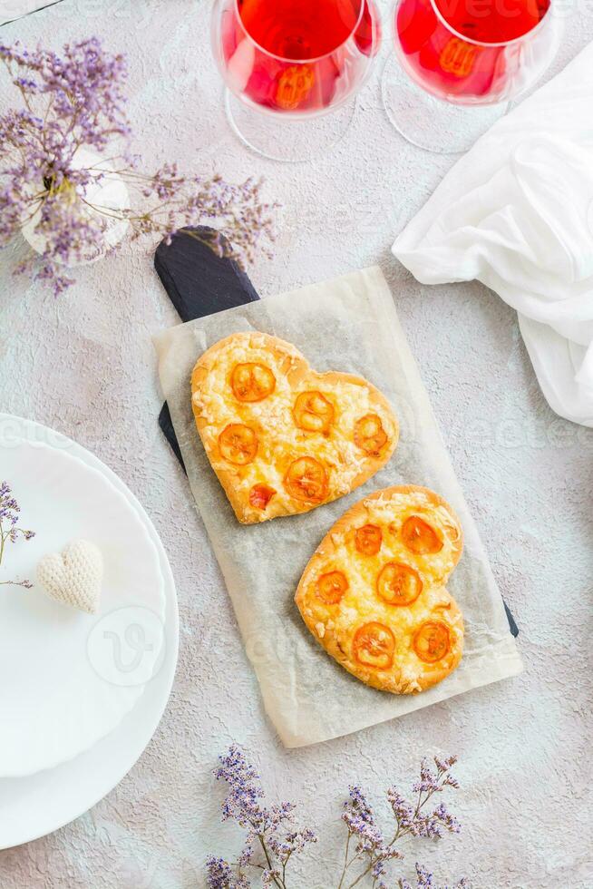 Two heart shaped pizzas on paper and two glasses of wine on a set table for valentine's day celebration. Top and vertical view photo