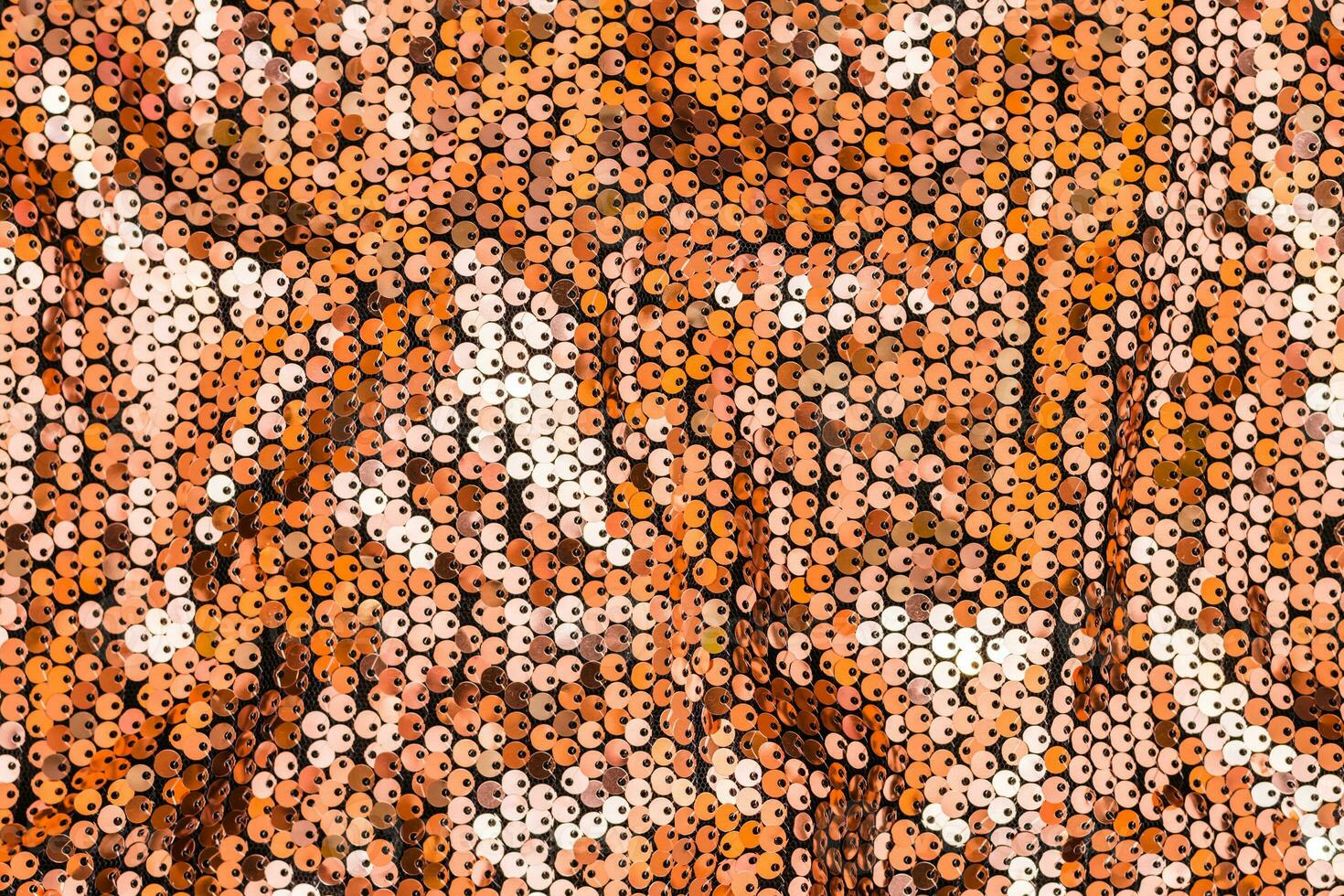 Textured gold background from round sequins on black fabric with waves. Top view photo
