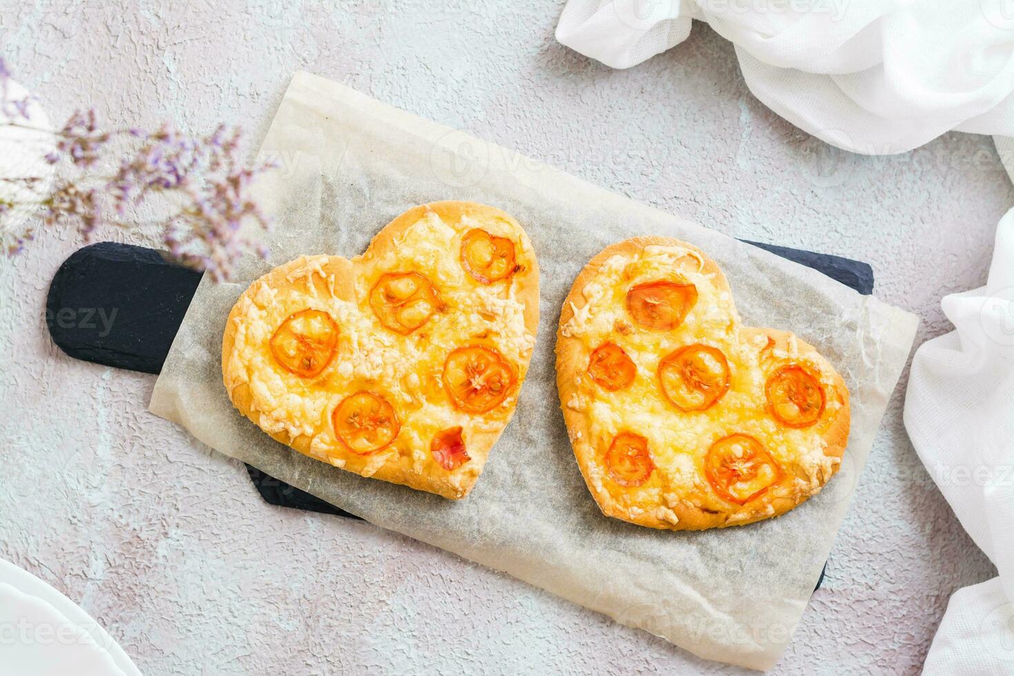 Two heart shaped ready-to-eat pizzas on paper on set table for valentine's day celebration. Close-up. Top view photo