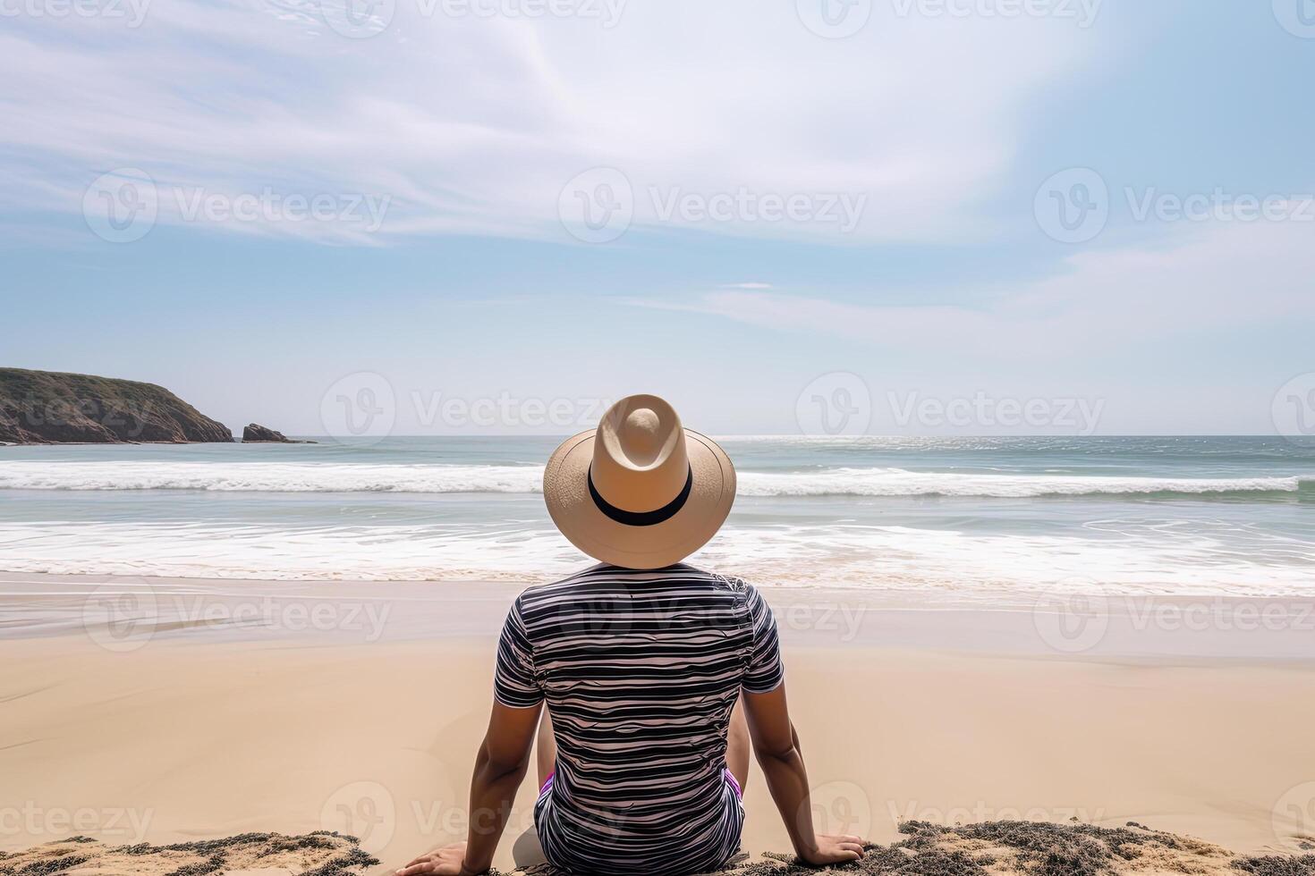 Back view of a man wearing a hat sitting on a beach. photo