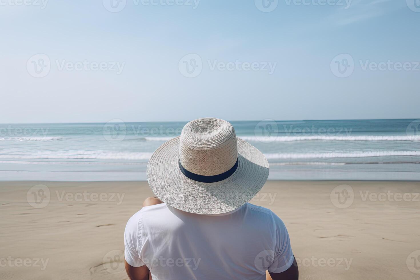 Back view of a man wearing a hat sitting on a beach. photo