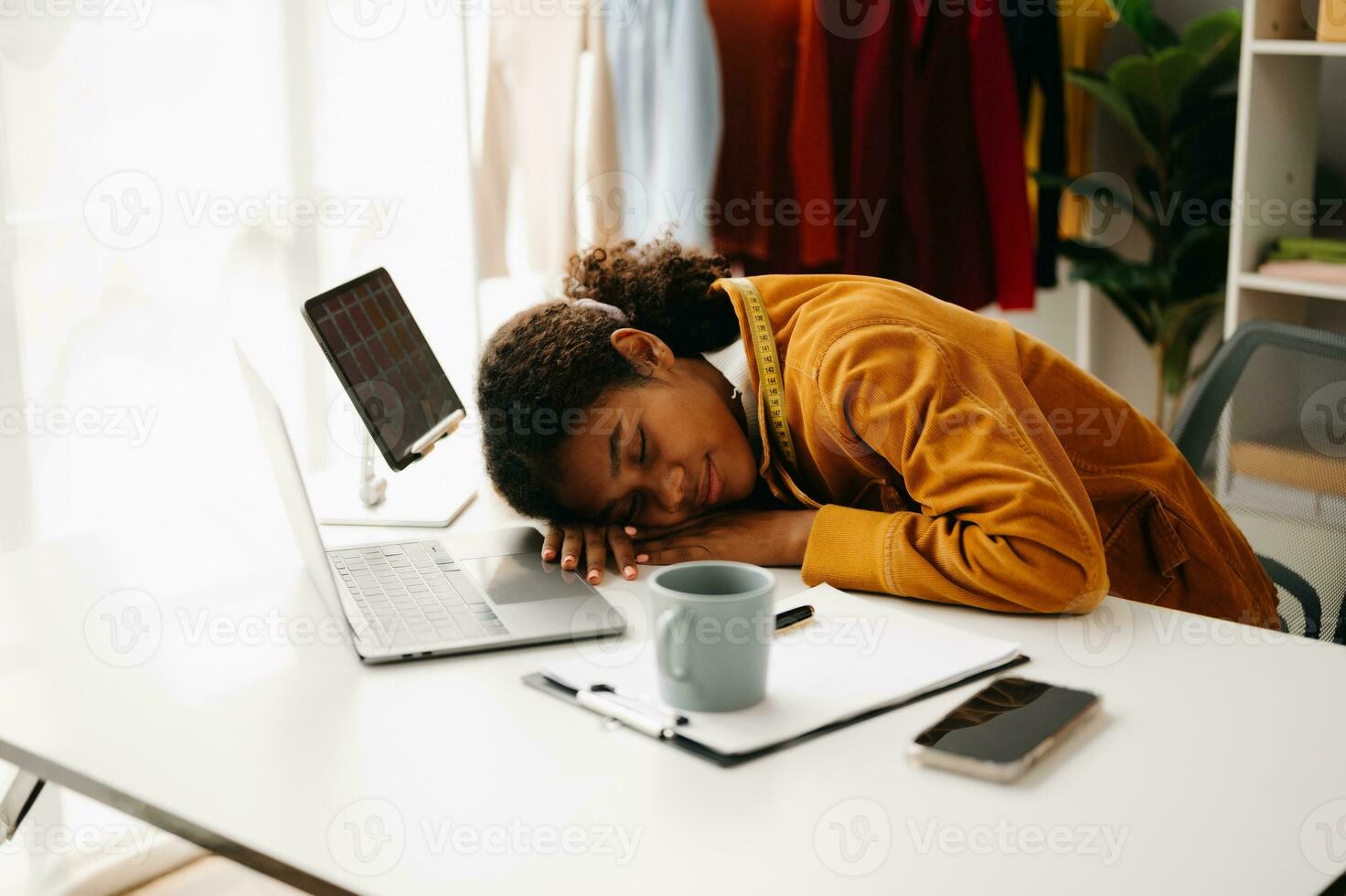 Calm curly brunette dark skinned woman on desk in office of fashion designer and holds tablet and smartphone. photo