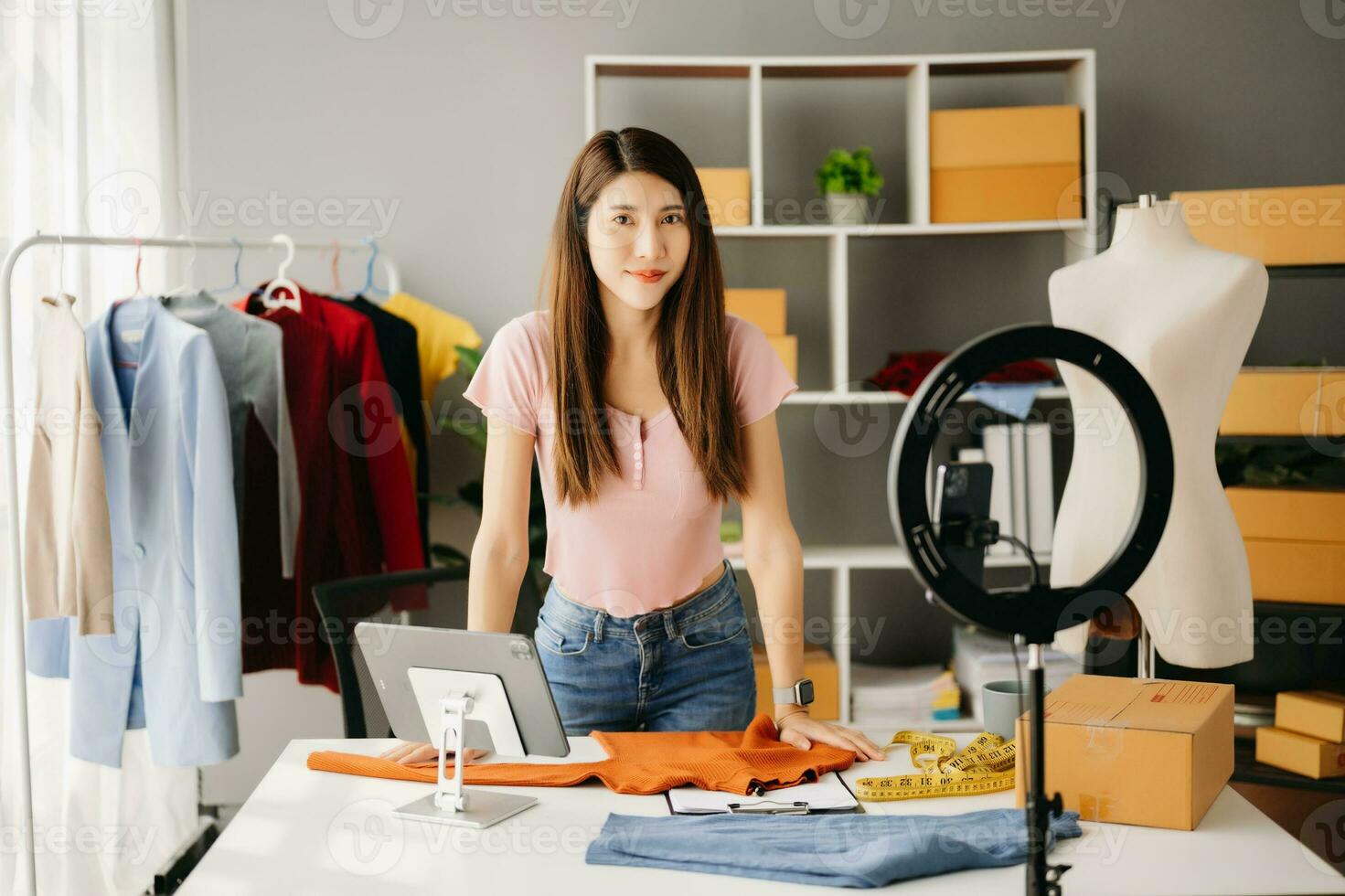 Fashion blogger concept, Young Asian women selling clothes on video streaming.Startup small business SME, using smartphone or tablet taking receive and checking photo
