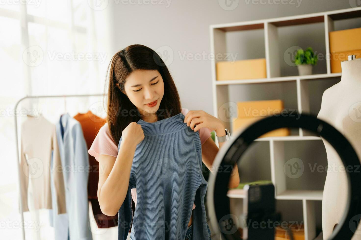 Fashion blogger concept, Young Asian women selling clothes on video streaming.Startup small business SME, using smartphone or tablet taking receive and checking photo