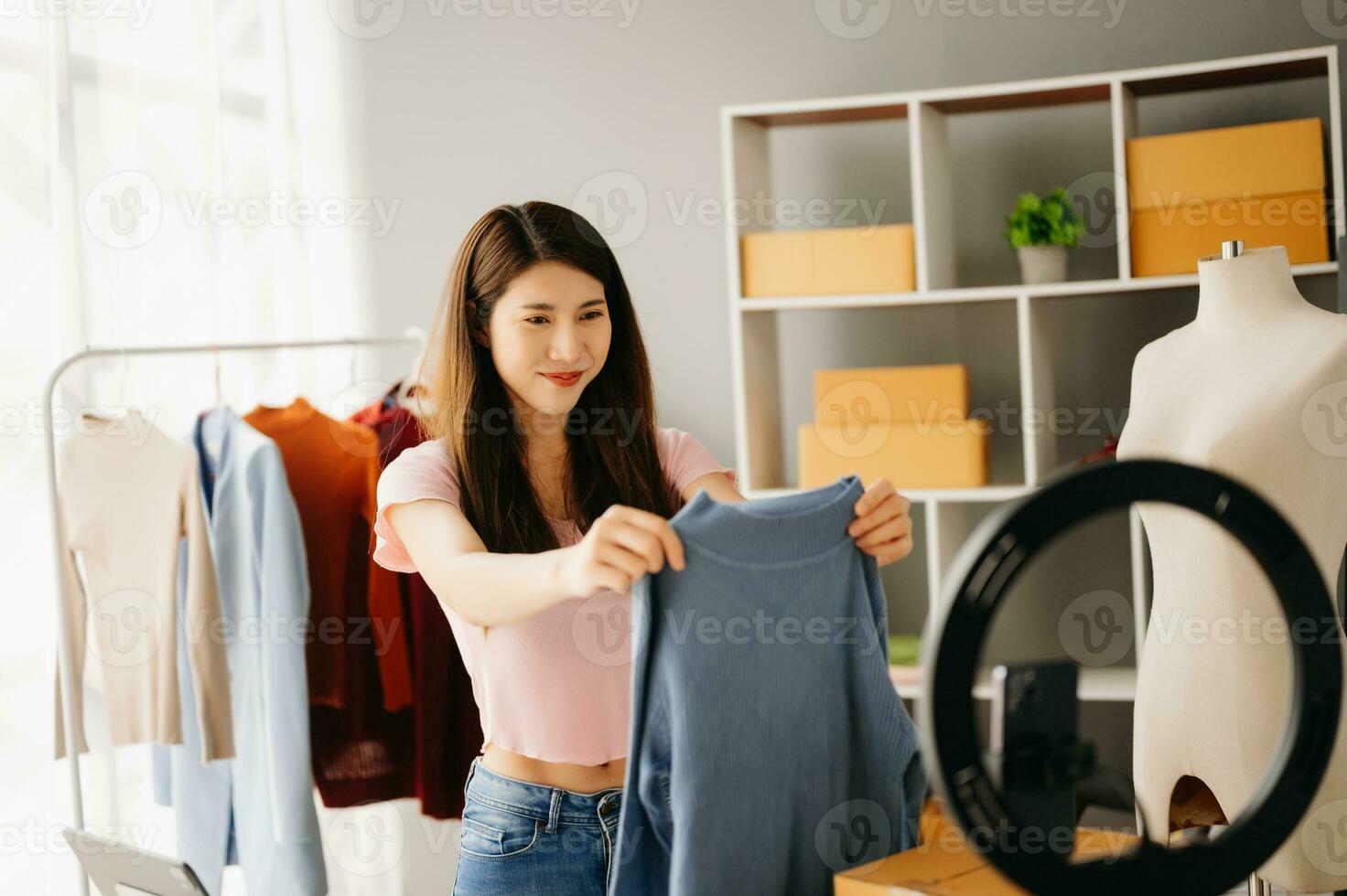 Fashion blogger concept, Young Asian women selling clothes on video streaming.Startup small business SME, using smartphone or tablet taking receive and checking photo