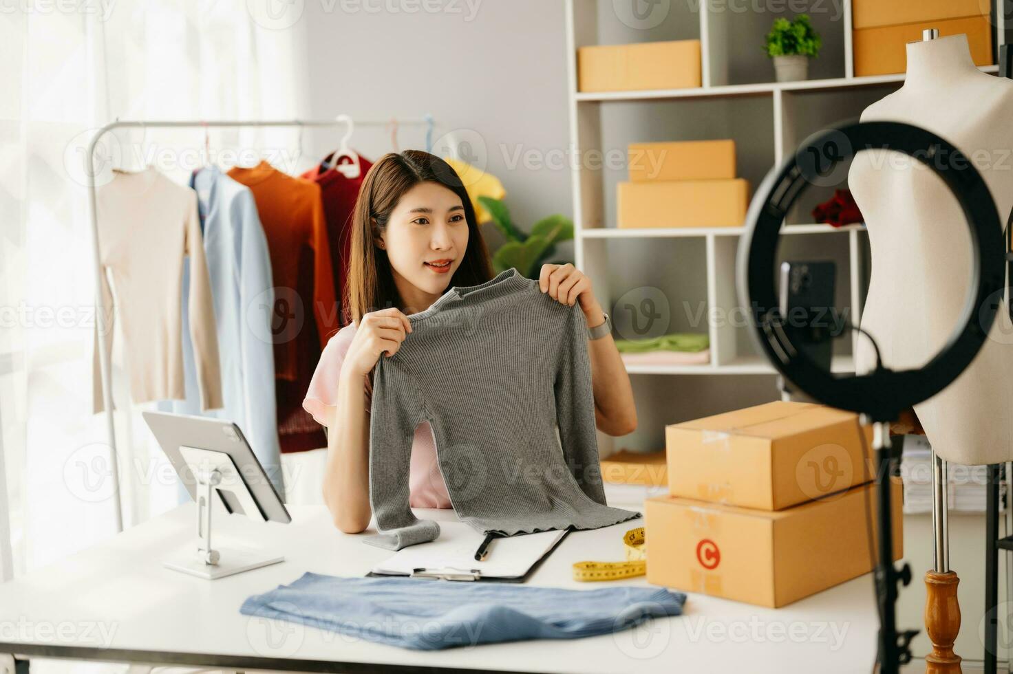 Fashion blogger concept, Young Asian women selling clothes on video streaming.Startup small business SME, using smartphone or tablet taking receive and checking photo