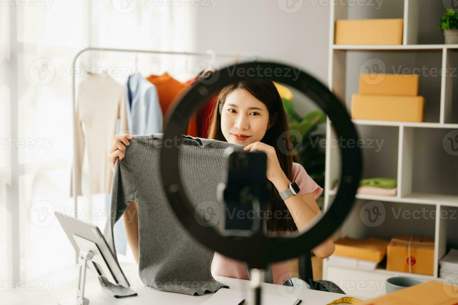 Fashion blogger concept, Young Asian women selling clothes on video streaming.Startup small business SME, using smartphone or tablet taking receive and checking photo